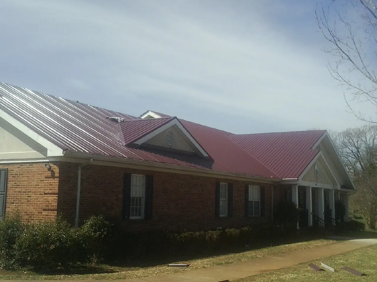 Red metal roof with gabled entries on a long brick building, from a Hail Damage Roof Repair job in Cascade Locks