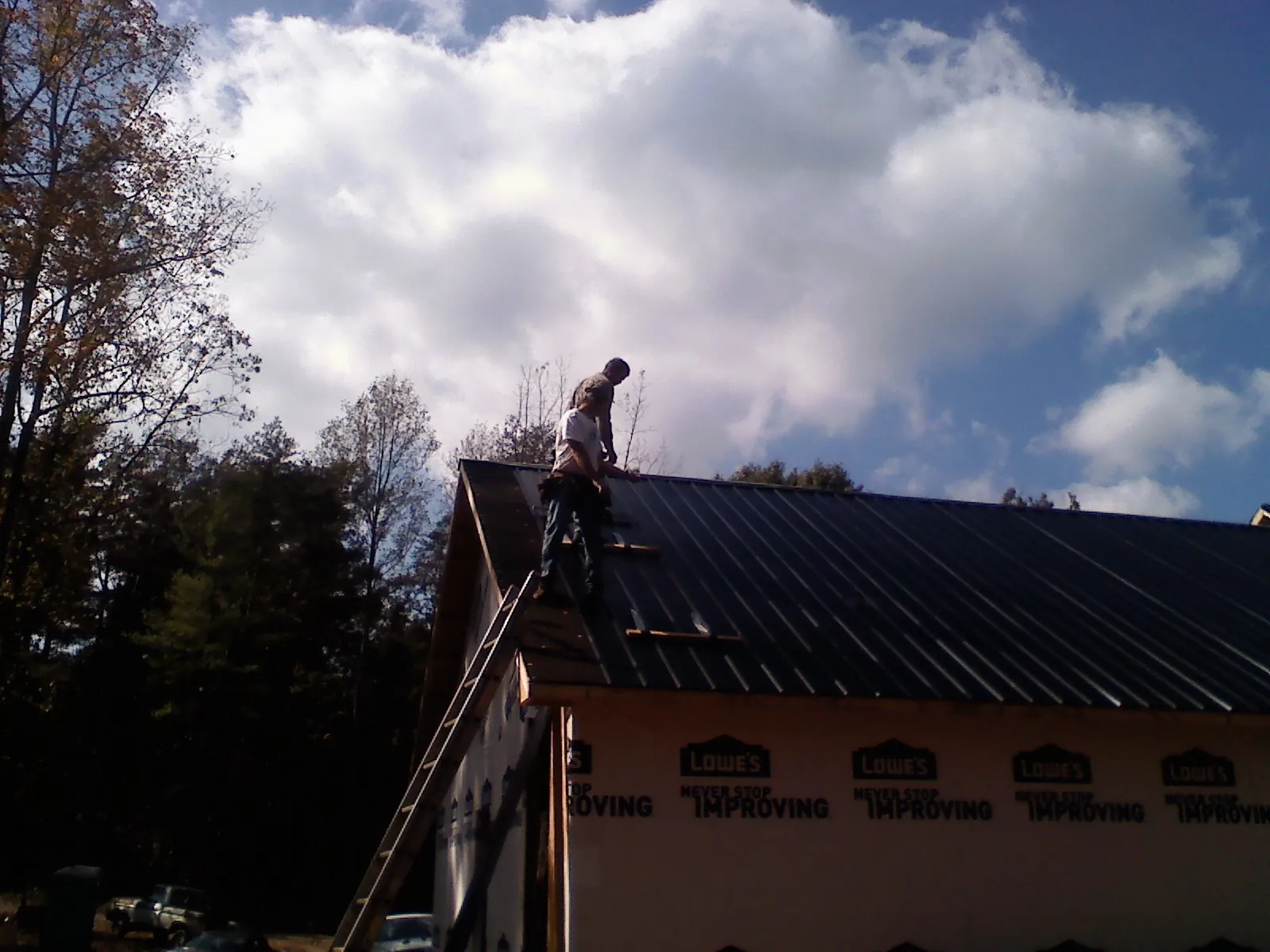Roofer fastening dark metal panels high against a cloudy sky, from a Roof Inspection job in Cascade Locks